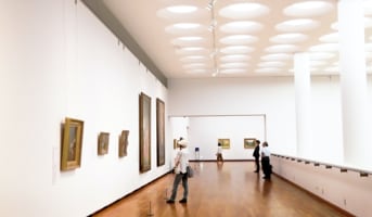 Room inside a gallery with pictures on walls and people looking at them.